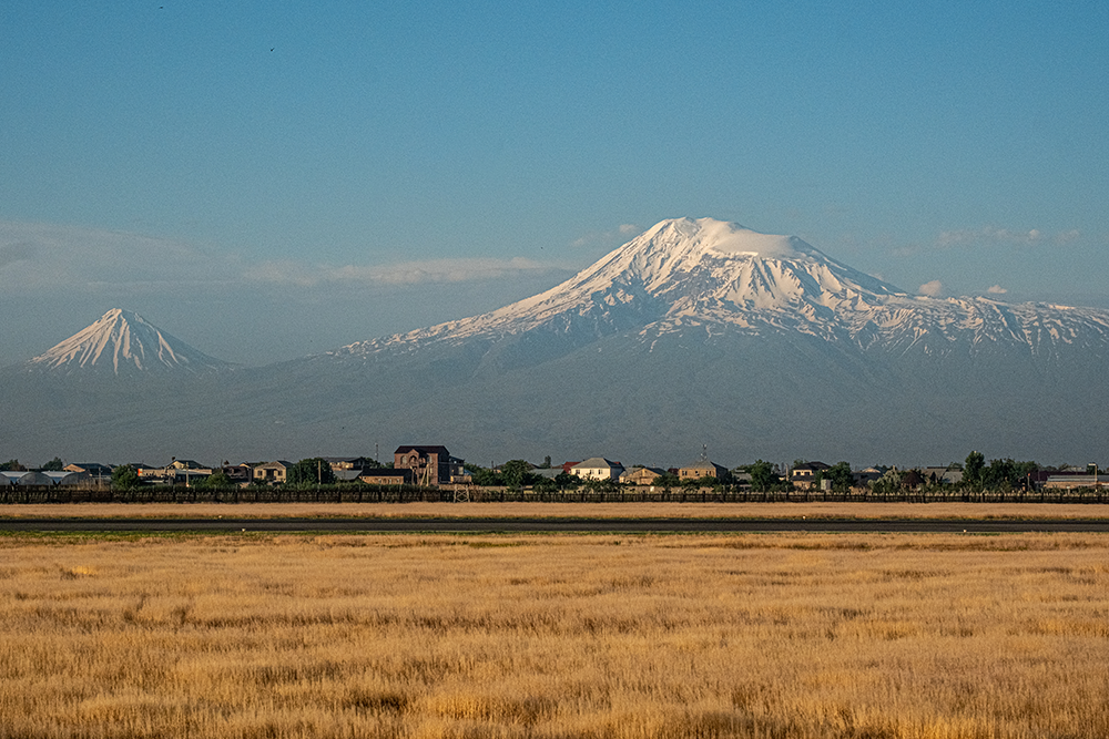 Scenic panoramic view of the snow-capped Mount Ararat and Little Ararat rising above rural houses, captured from Zvartnots International Airport.